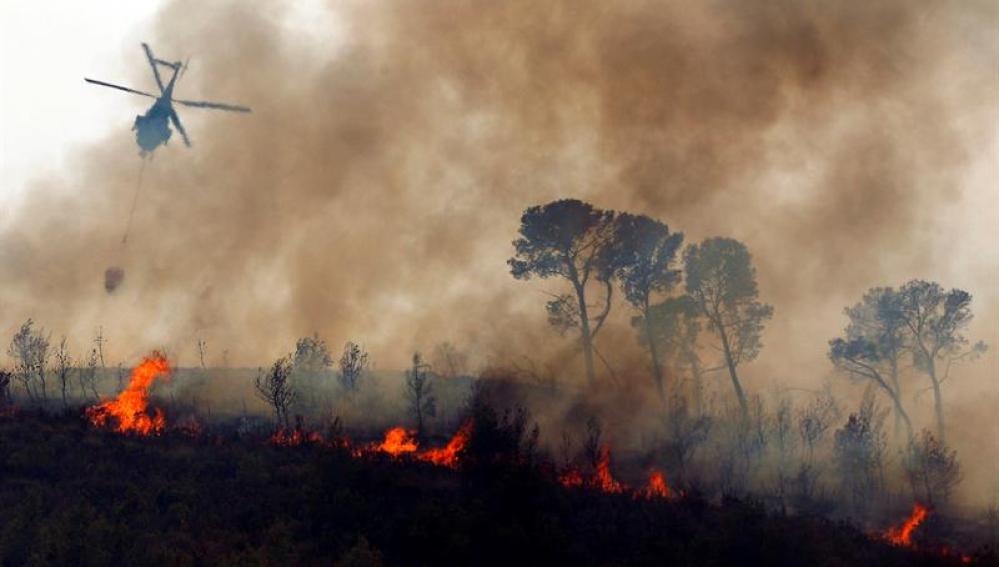 Un helicóptero vuela sobre el fuego durante los trabajos de extinción