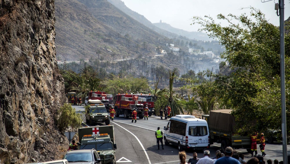 Varios coches de bomberos cortan el tráfico en el límite del incendio forestal en la isla 