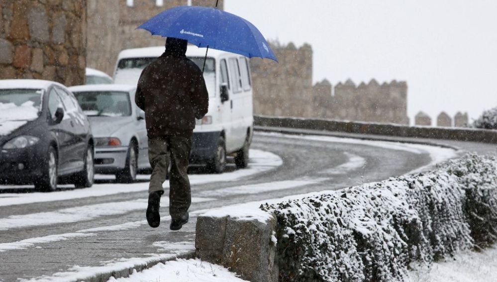 Un hombre corre con un paraguas para protegerse de la nieve en Ávila
