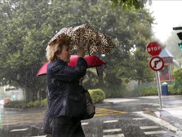 Una mujer se refugia del viento y la lluvia con el paraguas