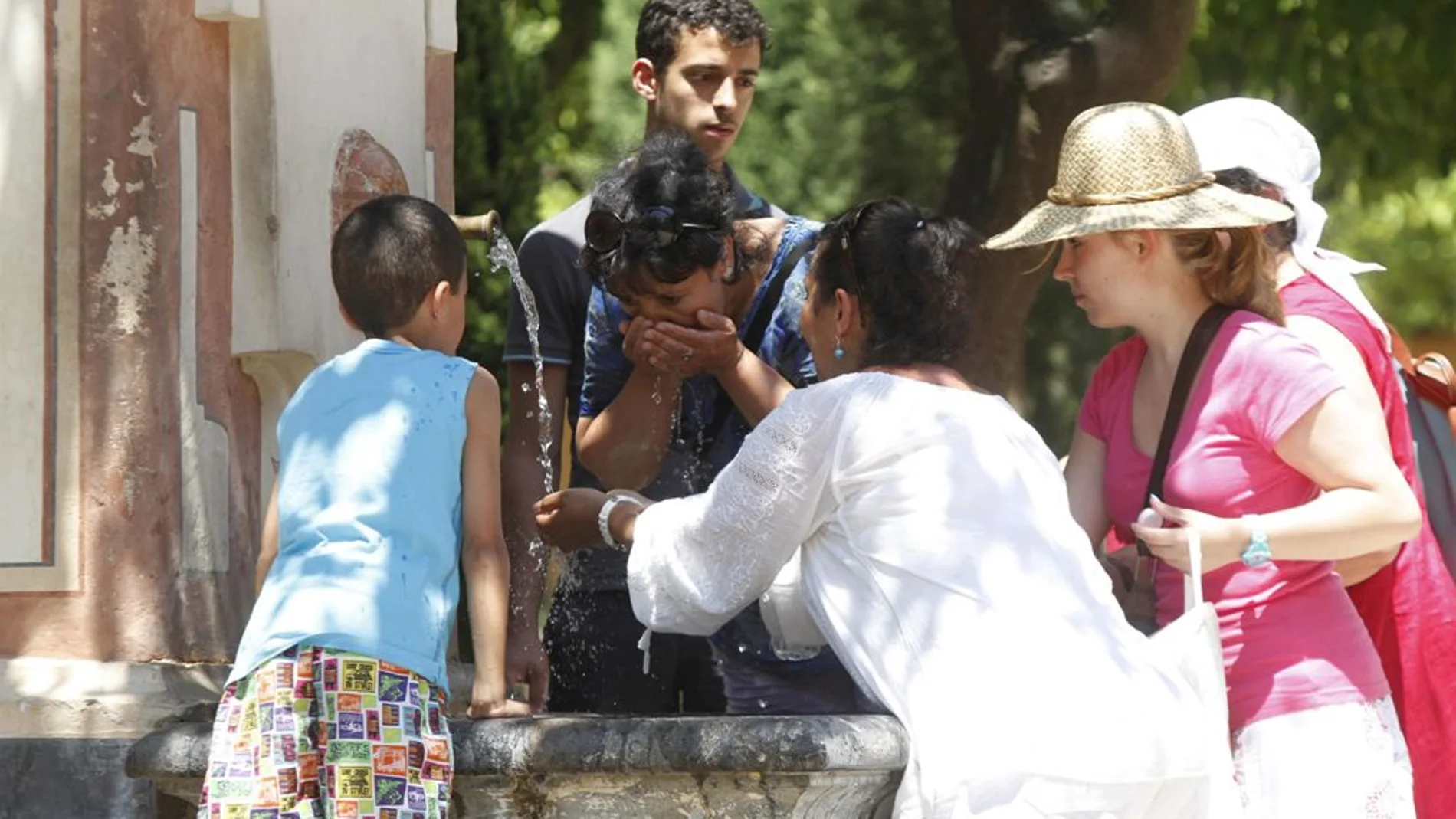 Un grupo de personas refrescándose en una fuente Un grupo de personas refrescándose en una fuente