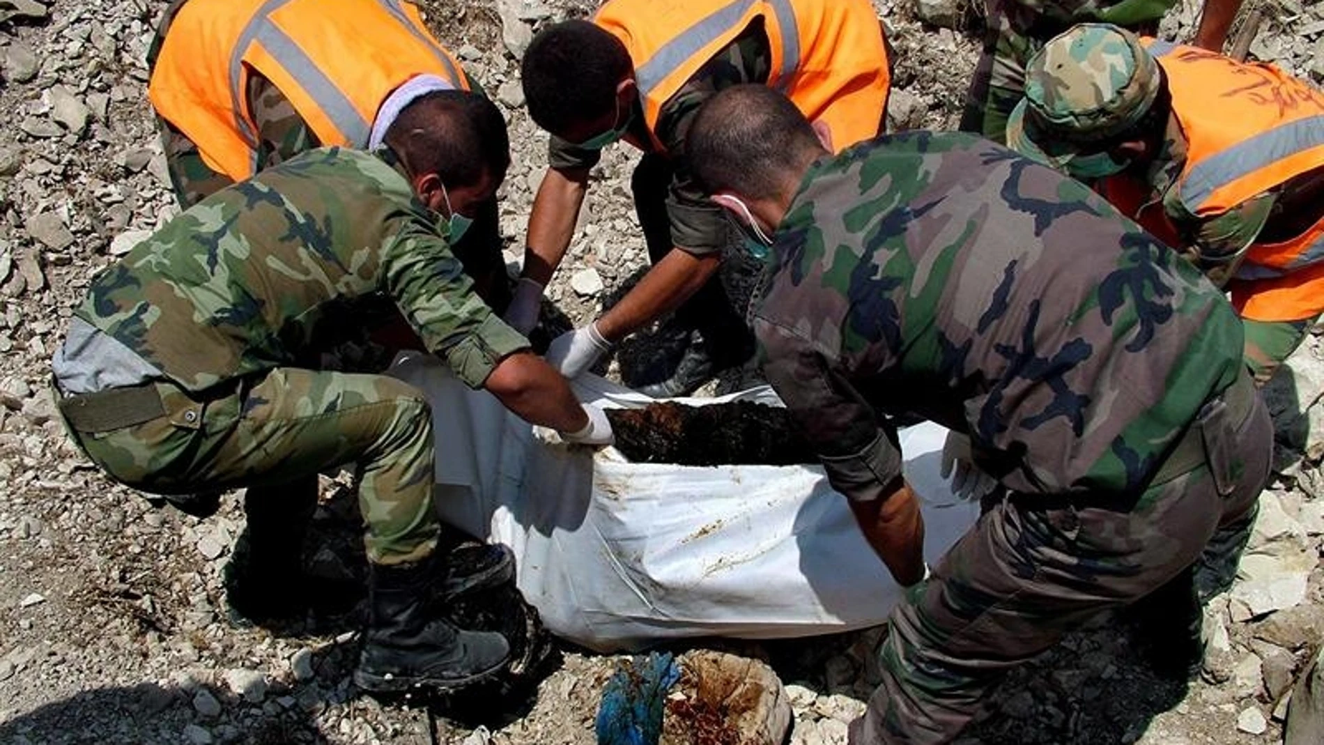 Miembros de la defensa civil de Siria removiendo un cuerpo de una tumba común Miembros de la defensa civil de Siria removiendo un cuerpo de una tumba común