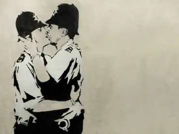 Obra de Banksy en blanco y negro, en la que aparecen dos policía británicos besándose. Obra de Banksy en blanco y negro, en la que aparecen dos policía británicos besándose.
