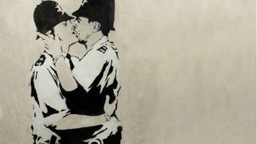 Obra de Banksy en blanco y negro, en la que aparecen dos policía británicos besándose.
