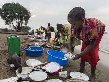 Un niño lava platos junto a un lago en el Congo