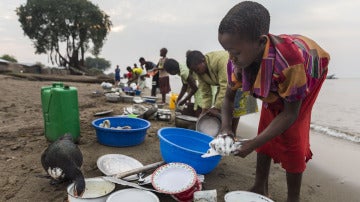 Un niño lava platos junto a un lago en el Congo