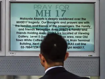 Un pasajero observa una pantalla en la que se lee "Rezo por MH17" Un pasajero observa una pantalla en la que se lee "Rezo por MH17"