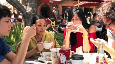 Tres personas consultan su tel&eacute;fono m&oacute;vil durante una comida