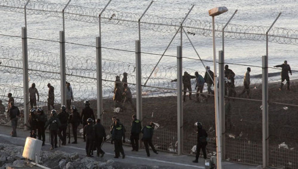 Las fuerzas españolas de seguridad e inmigrantes a ambos lado de la valla de Ceuta