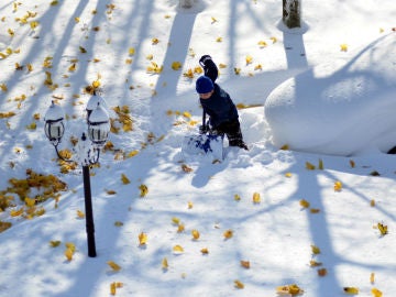 Un joven intenta retirar nieve junto a un coche cubierto de ella