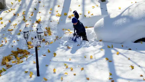 Un joven intenta retirar nieve junto a un coche cubierto de ella Un joven intenta retirar nieve junto a un coche cubierto de ella