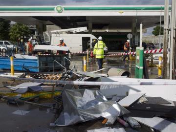 Empleados de una gasolinera retiran los desperfectos causados tras los fuertes vientos