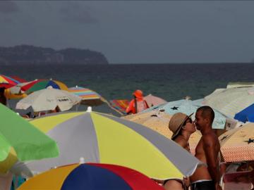 Dos bañistas entre sombrillas en una playa.