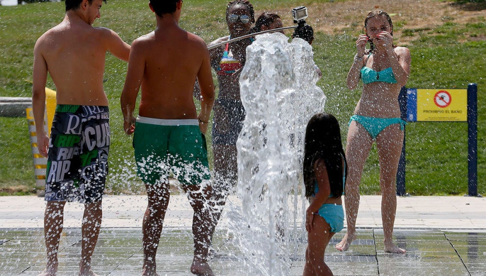 Jóvenes intentan aliviar el calor refrescándose en una de las fuentes del parque Juan Carlos I en Madrid