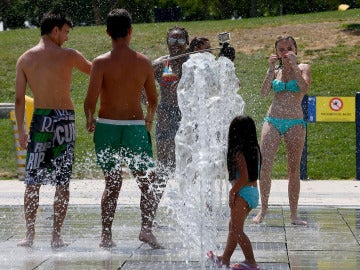 Jóvenes intentan aliviar el calor refrescándose en una de las fuentes del parque Juan Carlos I en Madrid