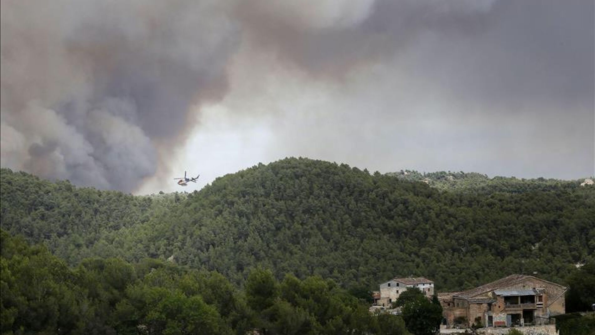 Un helic&oacute;ptero trabaja cerca de varias viviendas para combatir el incendio