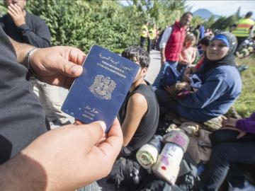 Un refugiado enseña su pasaporte sirio mientras espera para cruzar la frontera 