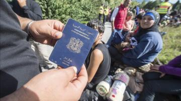 Un refugiado enseña su pasaporte sirio mientras espera para cruzar la frontera 