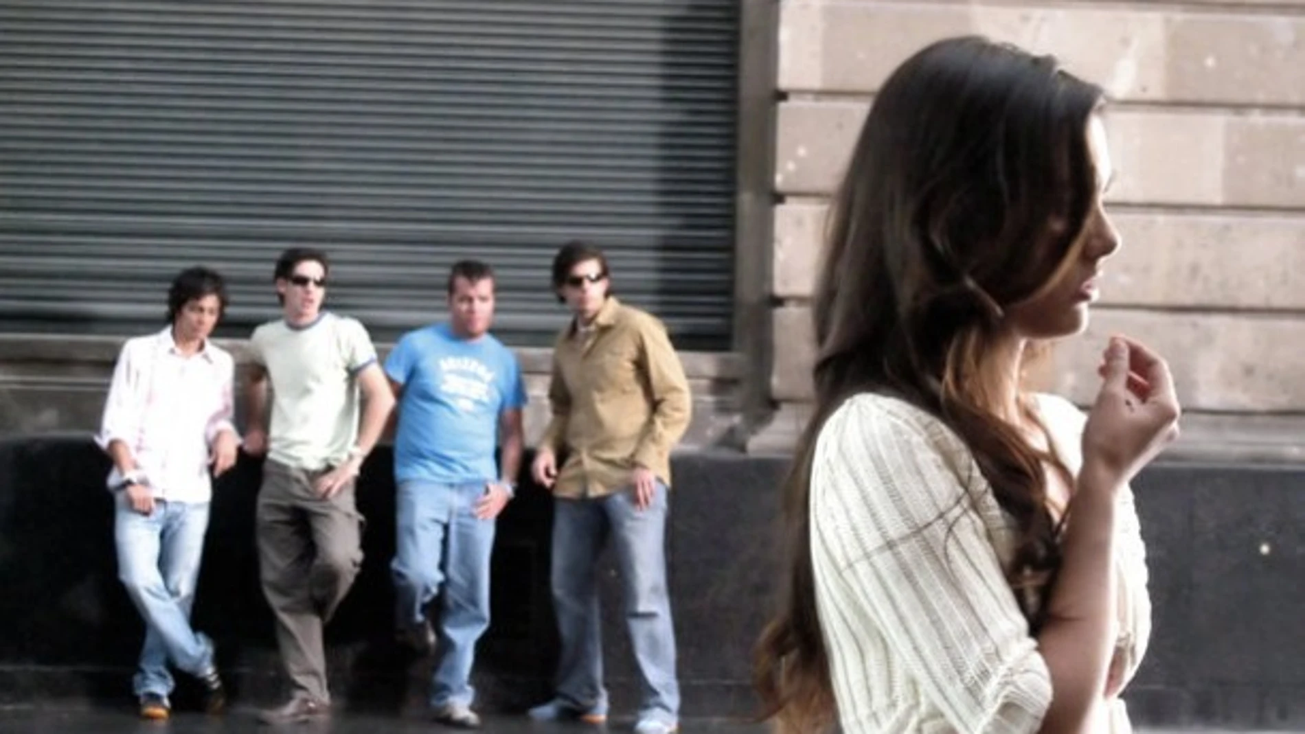 Un grupo de hombres observa a una mujer en la vía pública. Un grupo de hombres observa a una mujer en la vía pública.