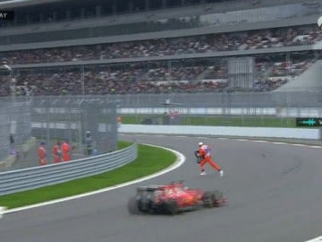 Un comisario retira la pieza del alerón de Carlos Sainz con Vettel justo detrás