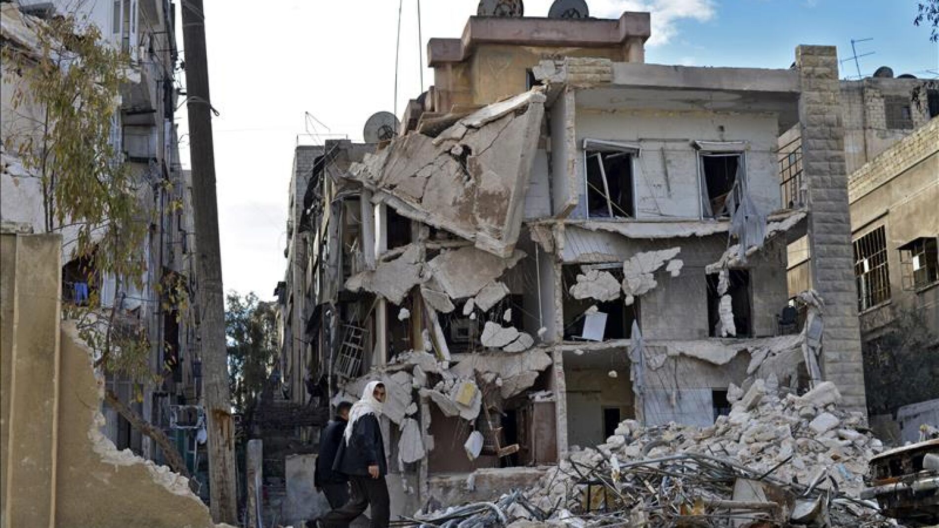 Varios civiles pasando por un edificio destru&iacute;do por los bombardeos en Alepo, Siria.