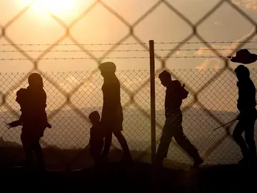 Varios inmigrantes caminan alrededor de una valla Varios inmigrantes caminan alrededor de una valla