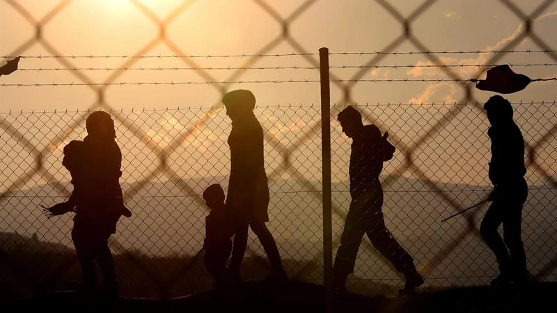 Varios inmigrantes caminan alrededor de una valla Varios inmigrantes caminan alrededor de una valla