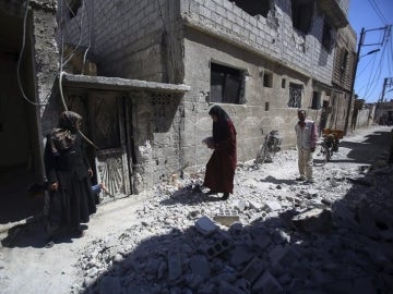 Varias personas inspeccionan edificios en ruinas tras los bombardeos en el pueblo de Deir al Asafi, al sureste de Damasco (Siria)