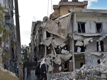 Varios civiles pasando por un edificio destruído por los bombardeos en Alepo Varios civiles pasando por un edificio destruído por los bombardeos en Alepo