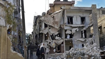 Varios civiles pasando por un edificio destruído por los bombardeos en Alepo