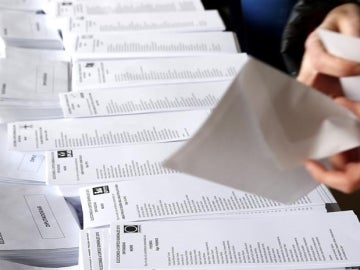  Una persona selecciona una de las papeletas dispuestas en el colegio electoral