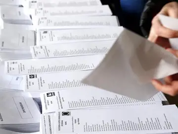 Una persona selecciona una de las papeletas dispuestas en el colegio electoral Una persona selecciona una de las papeletas dispuestas en el colegio electoral