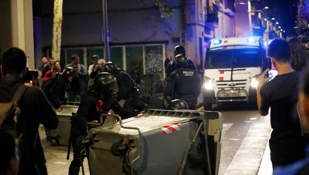 Varios antidisturbios retiran contenedores volcados en el barrio de Gràcia, en Barcelona