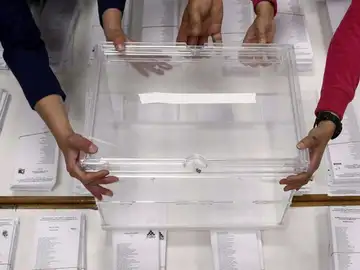 Varias manos sujetando una urna sobre las papeletas de unas elecciones Varias manos sujetando una urna sobre las papeletas de unas elecciones