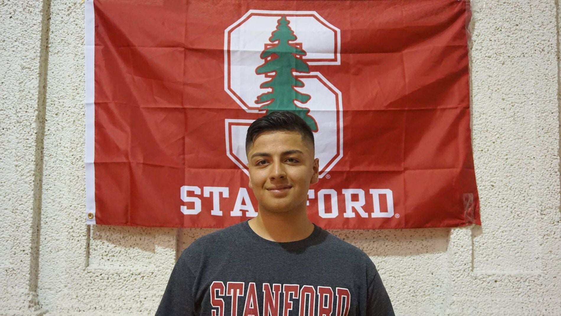 El joven junto a la bandera de su nueva universidad