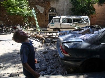 Un niño camina junto a vehículos y edificaciones dañados por un ataque aéreo