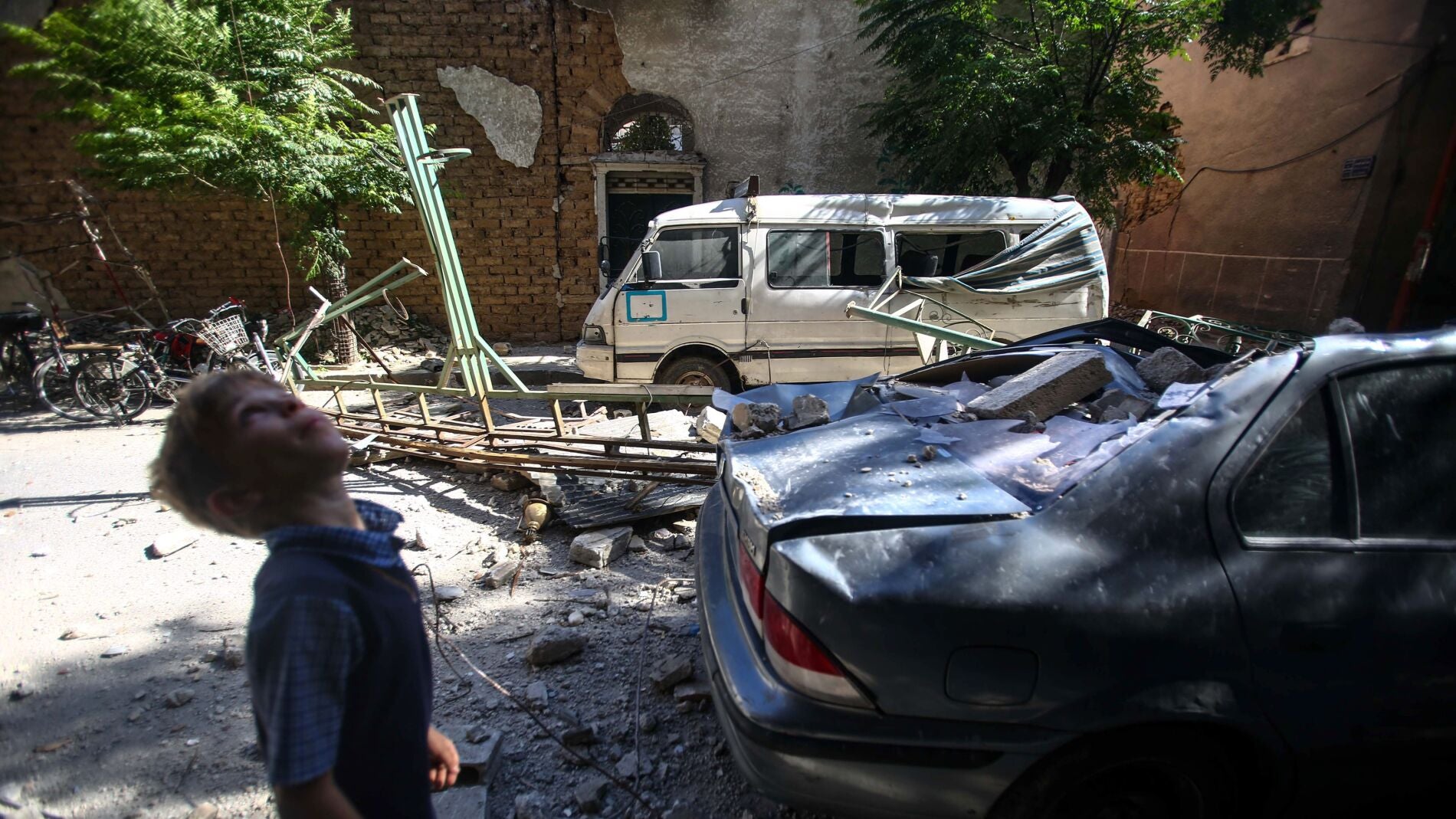Un ni&ntilde;o camina junto a veh&iacute;culos y edificaciones da&ntilde;ados por un ataque a&eacute;reo