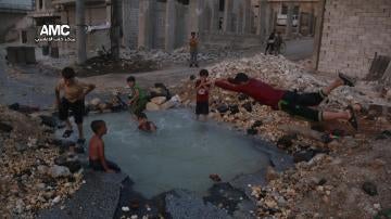 Un grupo de niños sirios juega en torno al cráter de una bomba convertido en piscina en Alepo