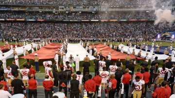 Colin Kaepernick, en la parte inferior de la fotografía (lleva el dorsal 7), de rodillas mientras suena el himno de Estados Unidos