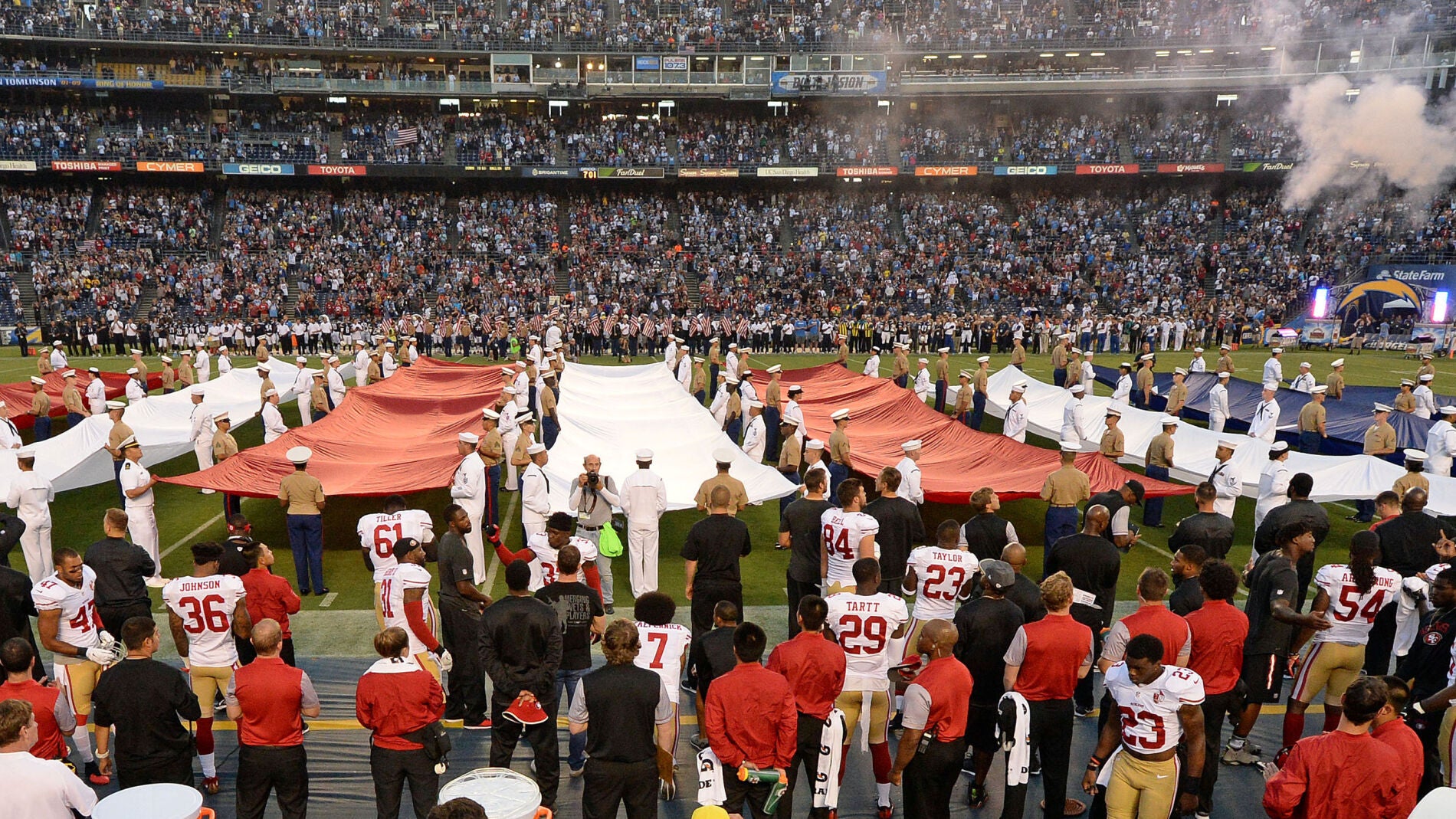 Colin Kaepernick, en la parte inferior de la fotograf&iacute;a (lleva el dorsal 7), de rodillas mientras suena el himno de Estados Unidos