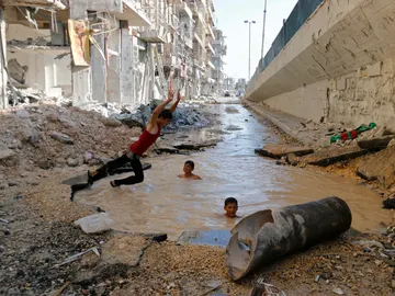 Un niño se sumerge en un cráter lleno de agua en el distrito de al-Shaar de Alepo. Un niño se sumerge en un cráter lleno de agua en el distrito de al-Shaar de Alepo.