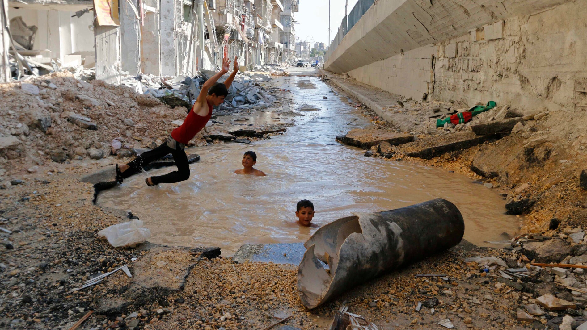Un ni&ntilde;o se sumerge en un cr&aacute;ter lleno de agua en el distrito de al-Shaar de Alepo.
