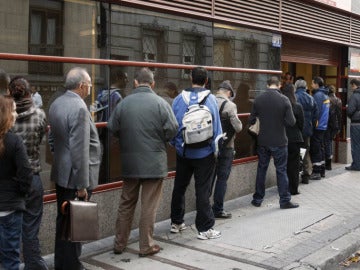 Varias personas hacen fila frente a una oficina de empleo
