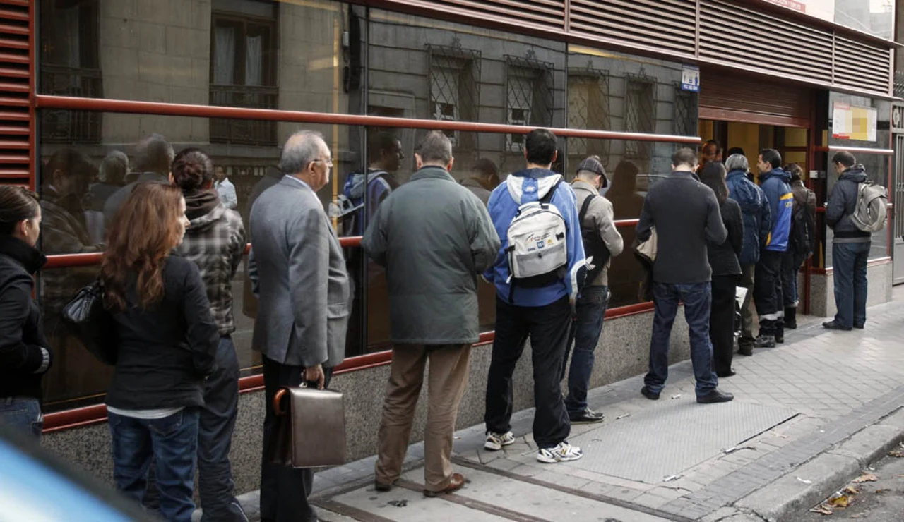 Varias personas hacen fila frente a una oficina de empleo