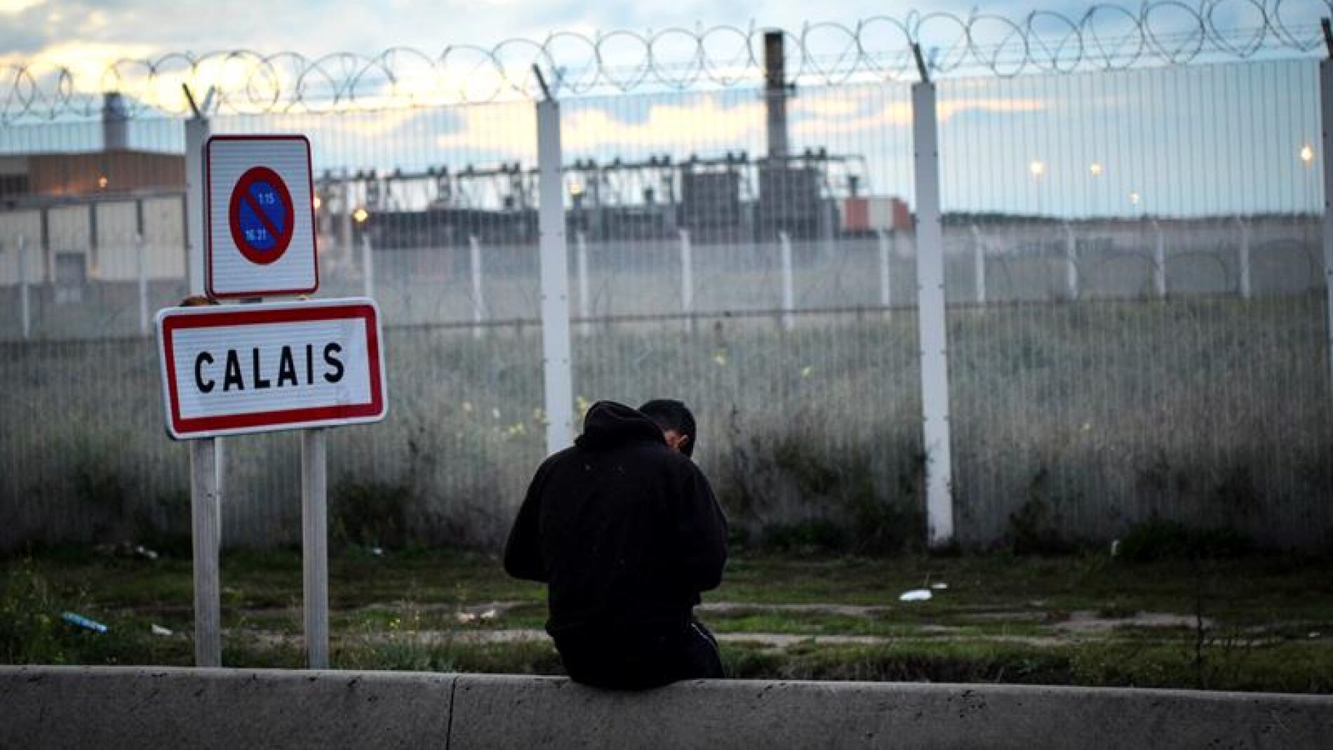 Un joven permanece sentado frente a una verja en del campamento de inmigrantes situado en Calais