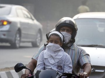 Un hombre y su hijo circulan en bicicleta protegidos con máscaras en Nueva Delhi