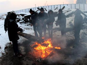 Varios refugiados se protegen del frío con una hoguera
