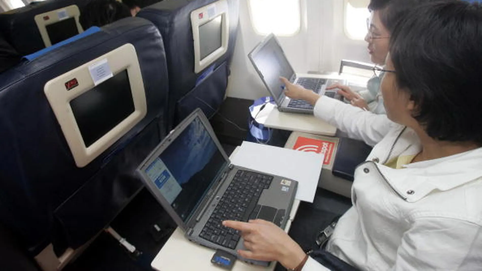 Dos pasajeros utilizando el ordenador portátil en un vuelo Dos pasajeros utilizando el ordenador portátil en un vuelo