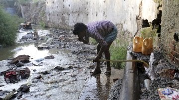 Un hombre bebe agua de una manguera conectada a la fuga de un oleoducto en Nueva Delhi