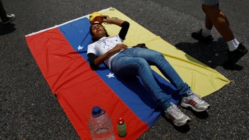 Una opositora protesta tumbada sobre la bandera de Venezuela